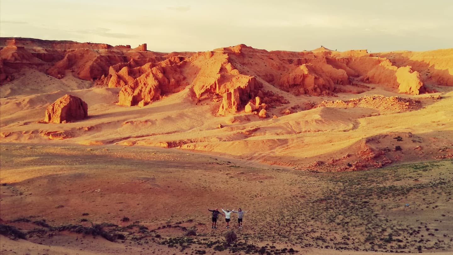Red sandstone rock formations at the Flaming Cliffs of Bayanzag glowing at sunset, with three people for scale