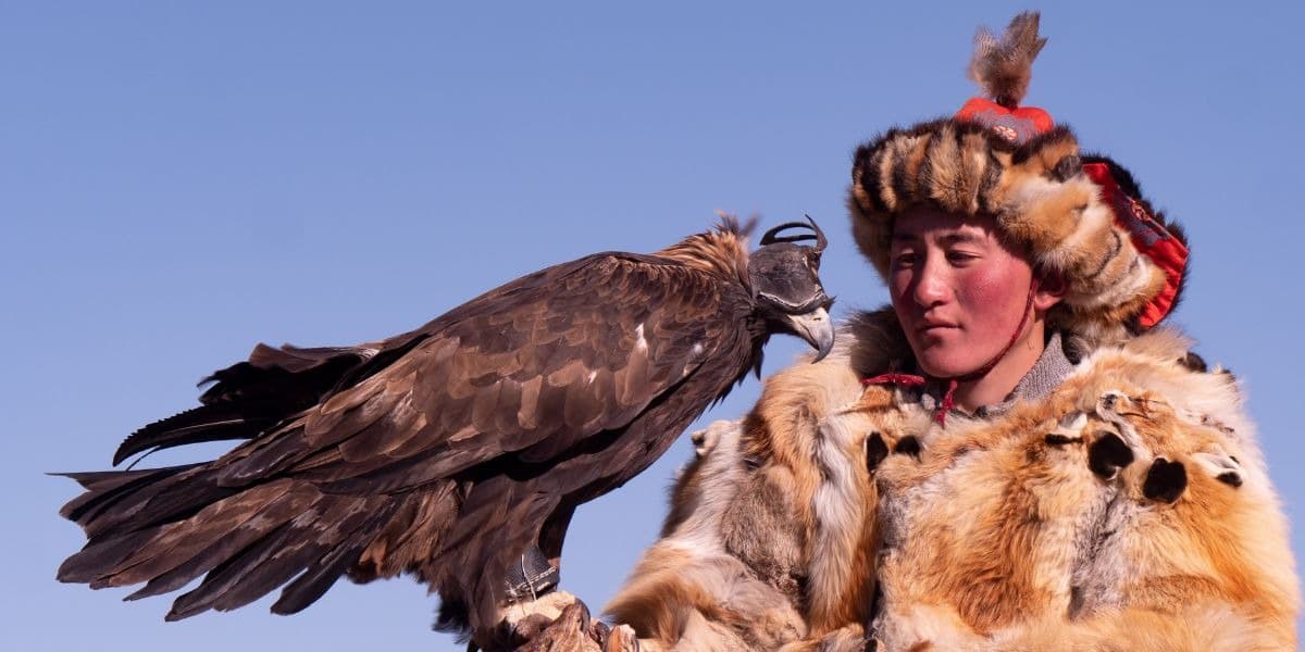 A Kazakh eagle hunter in traditional fur hat holding a golden eagle at the Golden Eagle Festival